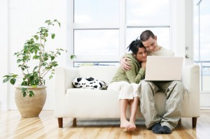 Couple cuddling on white couch looking at laptop