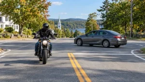 A helmeted motorcyclist approaches a New Hampshire intersection as a passenger car turns left across the rider's path.