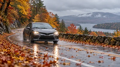 A passenger car travels on a wet New Hampshire road covered with autumn leaves.