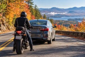 A motorcyclist stands safely beside a stopped motorcycle after a rear-end collision on a New Hampshire road.